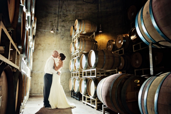 Bride and groom kissing in wine cellar barrels