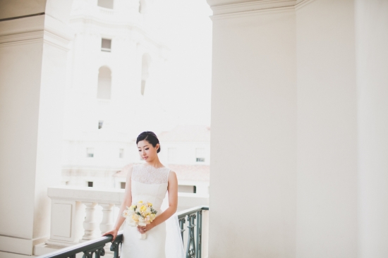 Elegant bride in white dress holding bouquet on a balcony