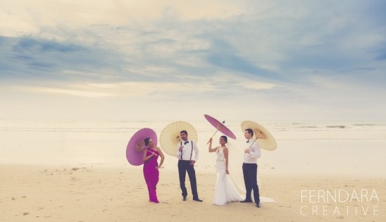 Bride groom wedding party holding parasols on the beach