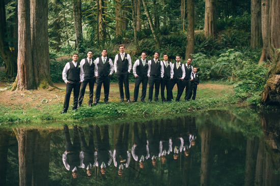 Groomsmen posing by a lake with reflections in a forest setting