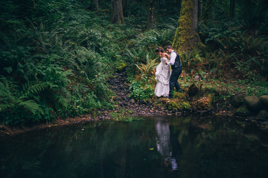Couple in wedding attire near forest pond, reflecting in water