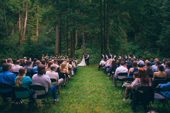 Outdoor wedding ceremony in a lush forest setting with guests seated
