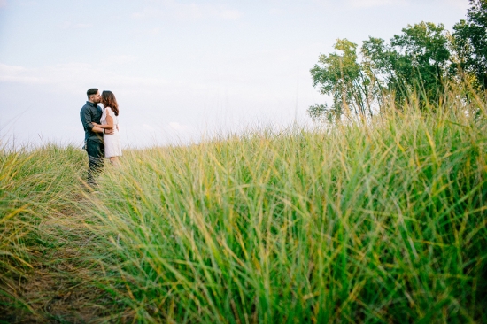 Couple embracing in a field of tall grass under a bright sky