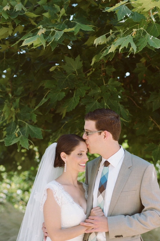 Groom kissing bride's forehead under a tree
