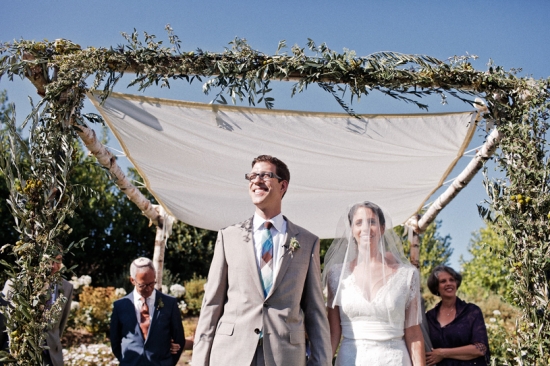 Happy couple exchanging vows under a floral chuppah