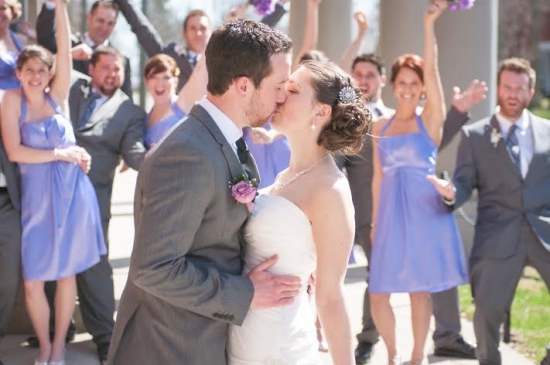 Bride and groom kissing surrounded by wedding party