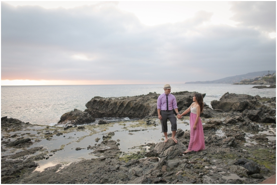 Couple holding hands on a rocky shore at sunset