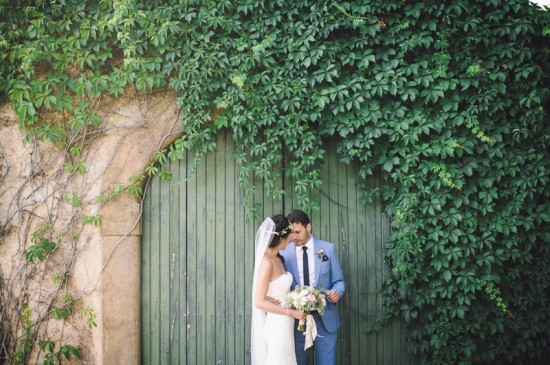 Bride and groom embrace by a wall covered in ivy