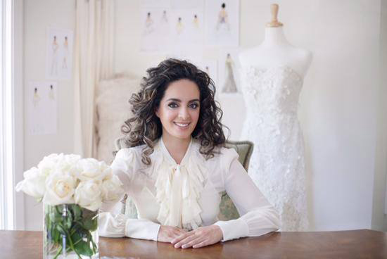 Smiling fashion designer at her desk with bridal gown, elegant style