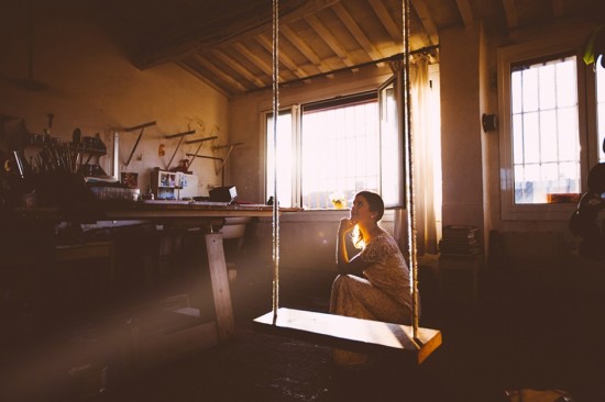 Woman sits on swing in sunlit artist studio