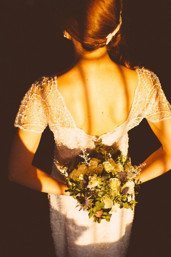 Bride in lace gown holds floral bouquet behind her back