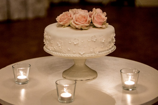 Elegant white cake topped with roses surrounded by candles