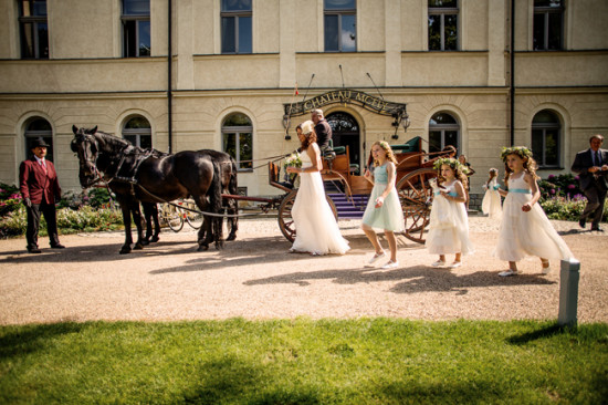 Bride and flower girls walk from horse carriage at chateau wedding