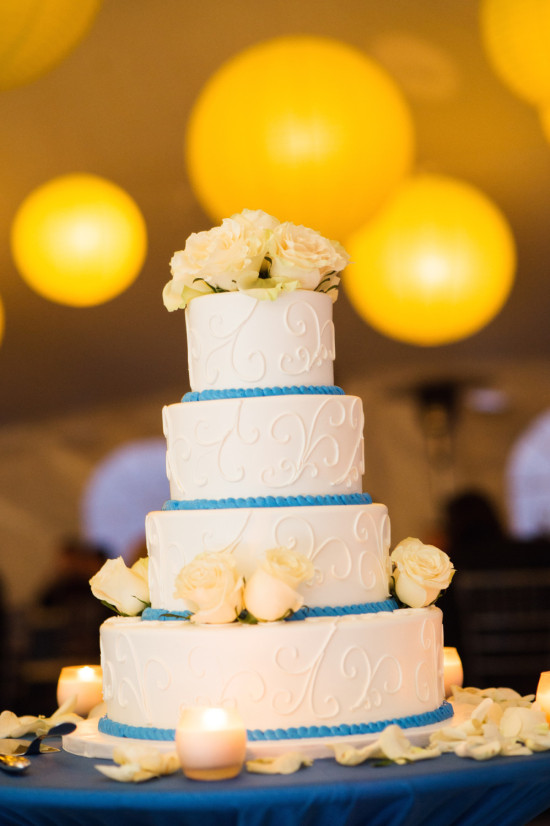 Elegant tiered white wedding cake with blue trim and roses