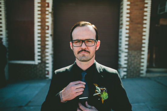 Groom adjusts tie wearing glasses and a boutonniere