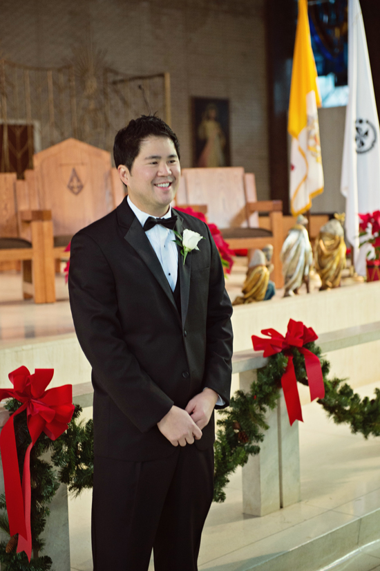 Groom in tuxedo smiles in a church decorated for Christmas