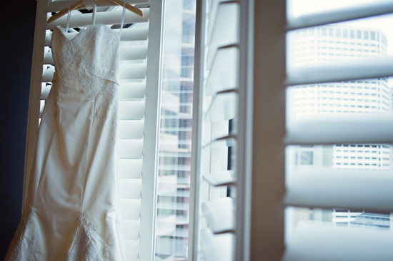 Wedding gown hanging by a shuttered window ready for the bride