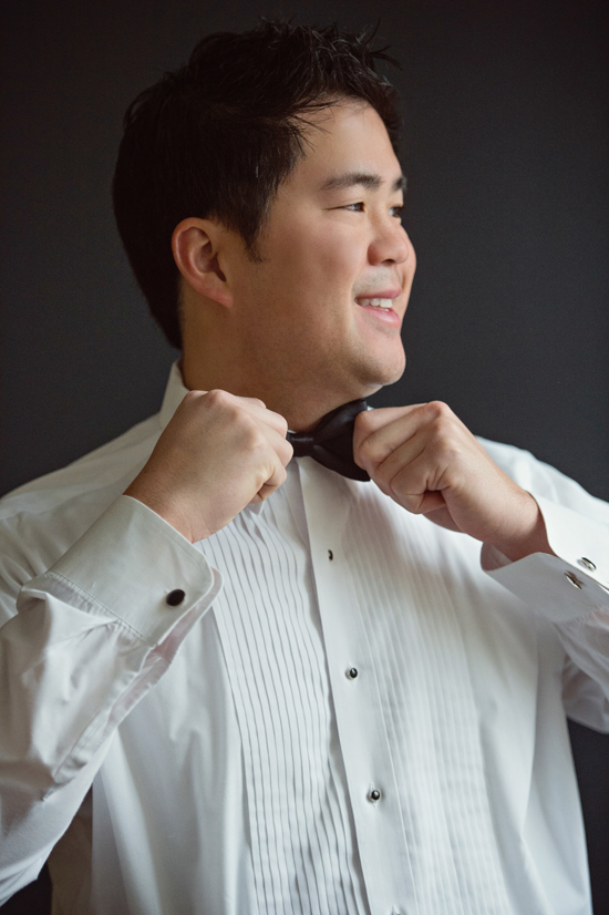 Smiling groom adjusts his black bow tie for the wedding