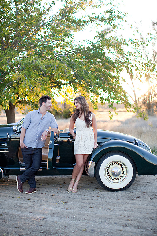 Couple leaning on classic car, looking at each other with affection