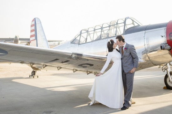 Newlyweds share a kiss in front of a vintage airplane