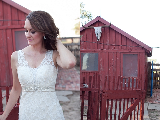 Bride in lace dress poses near rustic red barn