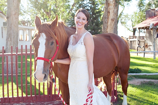 Bride poses with a horse at a ranch wedding in sunny weather