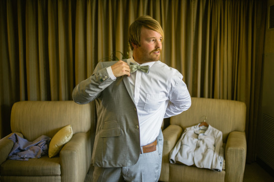 Groom adjusts bowtie, preparing for his wedding in the hotel room