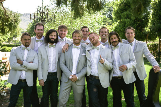 Groomsmen group photo smiling in suits at an outdoor wedding