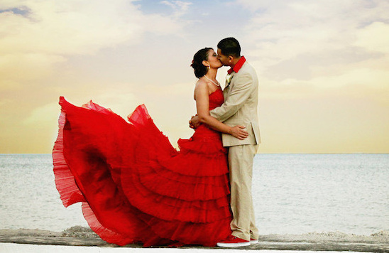 Wedding couple embracing and kissing on the beach, red dress
