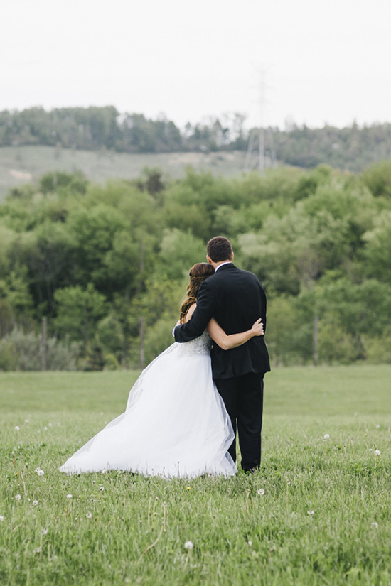 Bride and groom embrace overlooking a green field view