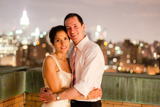 Couple embraces with NYC skyline in the background, at night