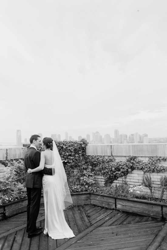 Elegant bride and groom embrace on rooftop with city skyline view
