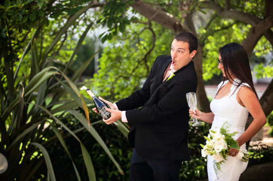 Groom popping champagne at wedding with his surprised bride
