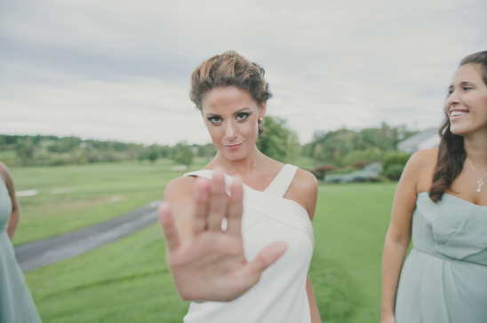 Bride playfully blocking the camera at outdoor wedding event