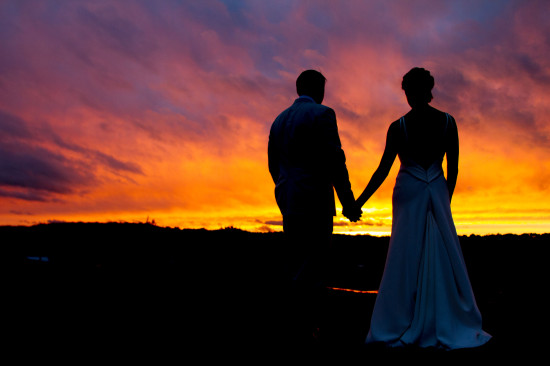 Couple holding hands silhouetted against a sunset sky