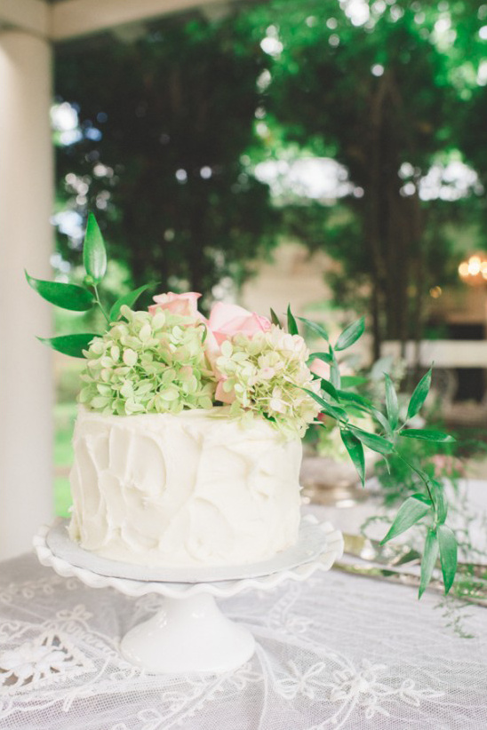 White cake with pink roses and green hydrangeas on stand