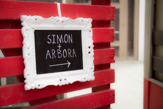 Simon and Arbora directional wedding sign on red wood fence