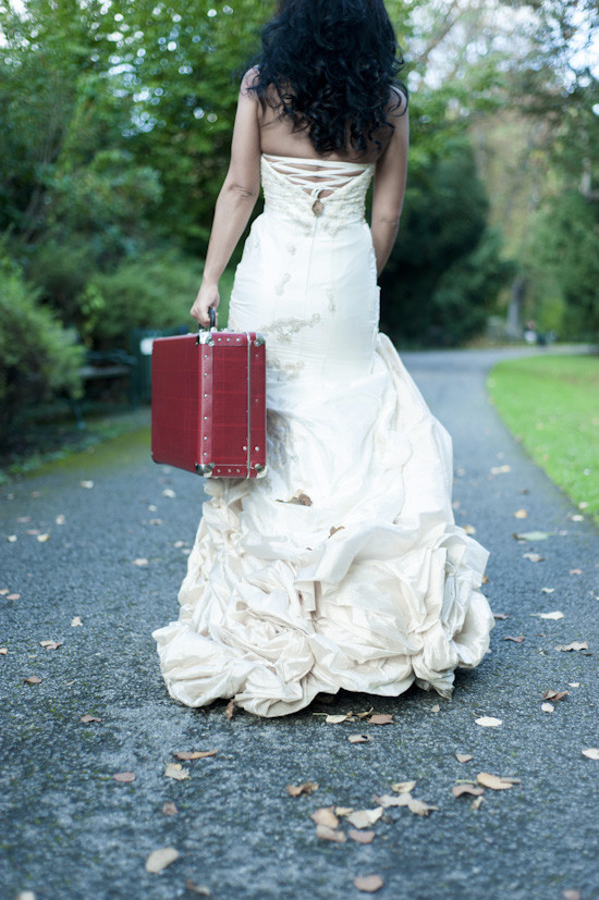 Bride walks away in wedding dress with red suitcase
