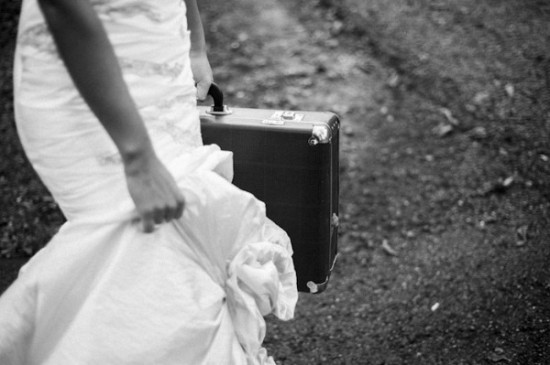 Bride in wedding dress carrying suitcase leaving the path