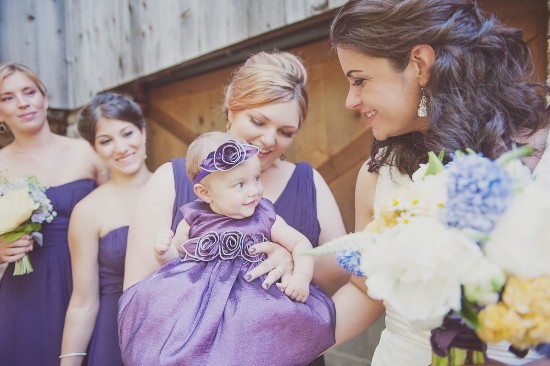 Baby girl in purple dress with bridesmaids smiling around her