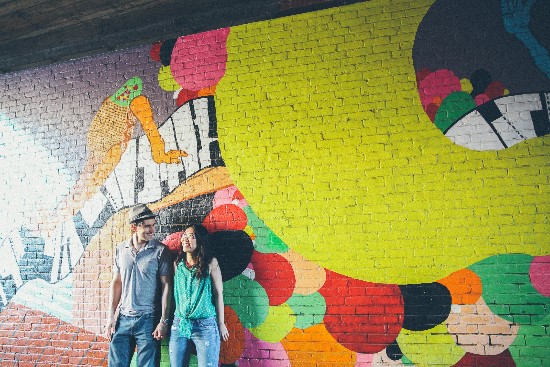 Couple stands before colorful mural on brick wall
