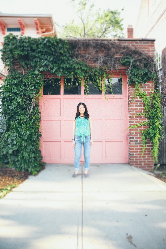 Young woman standing in front of a pink garage door with vines