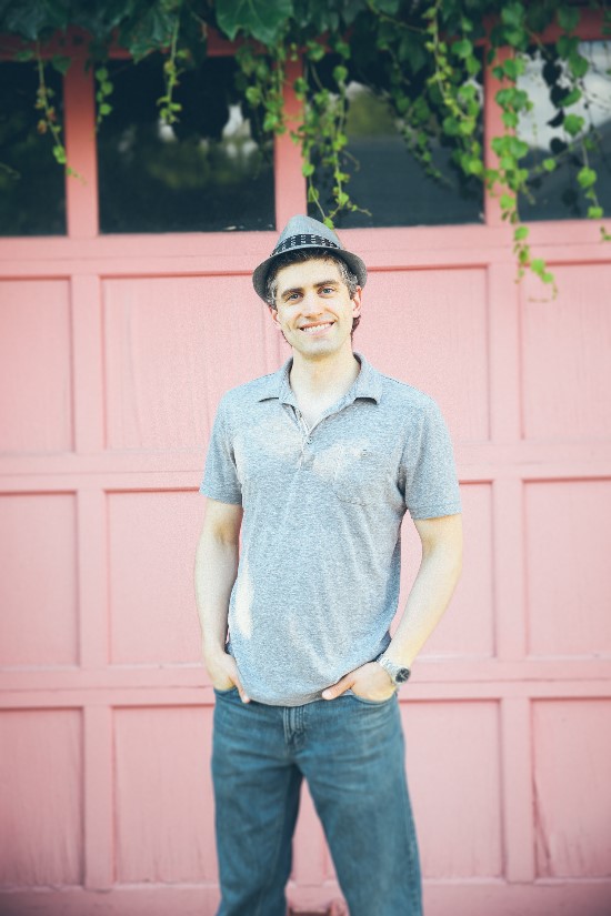 Smiling man wearing a hat standing in front of pink door