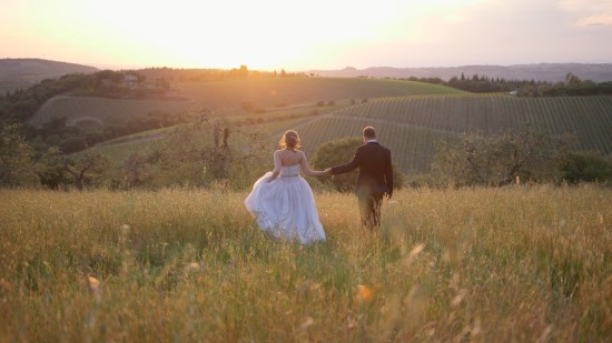 Wedding couple walking through field at sunset