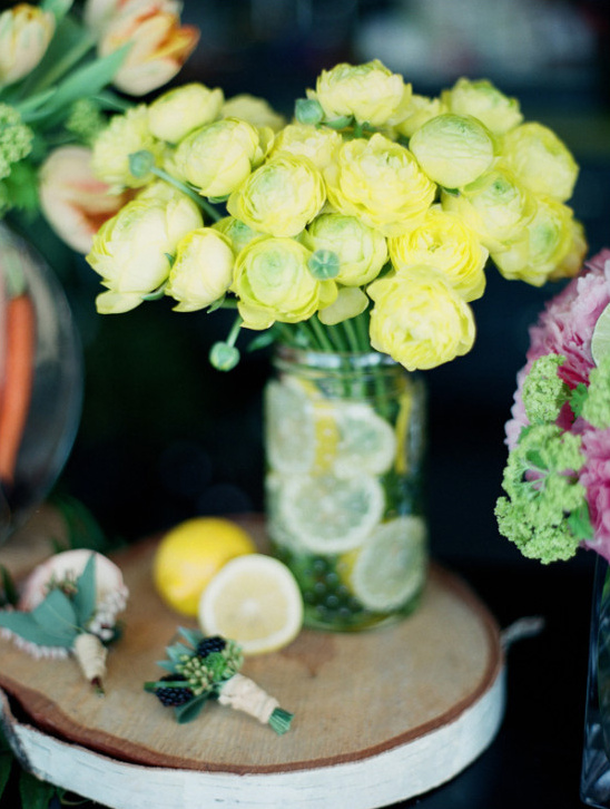 Yellow flowers with lemons in a jar centerpiece on a wooden slice