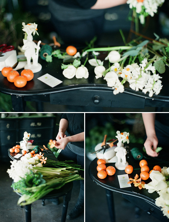 Florist arranging white flowers and oranges on a black table