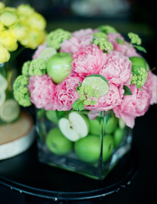 Pink floral arrangement with apples and limes in a glass vase