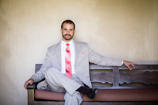 Man in light suit and pink tie poses on wooden bench