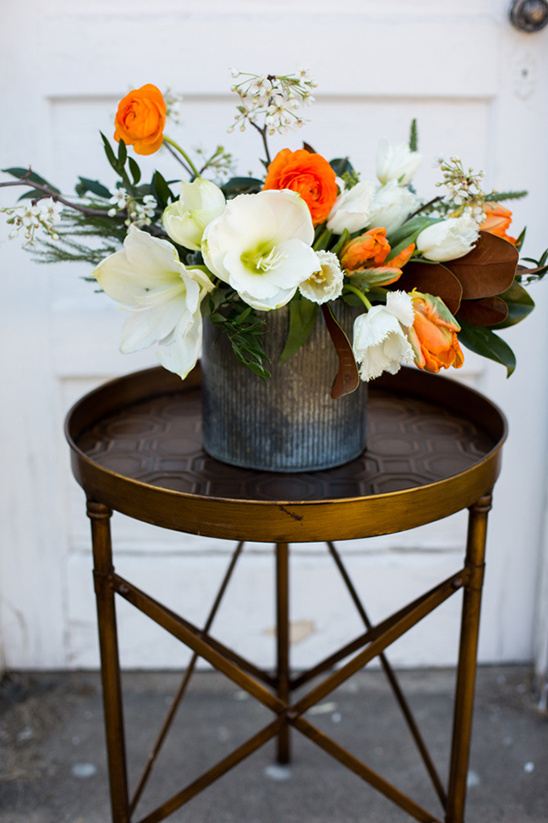 Orange and white flowers in metal vase on gold table