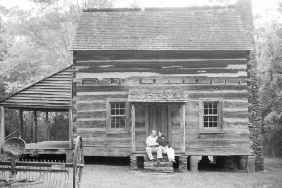 Couple sits on porch of a vintage log cabin house